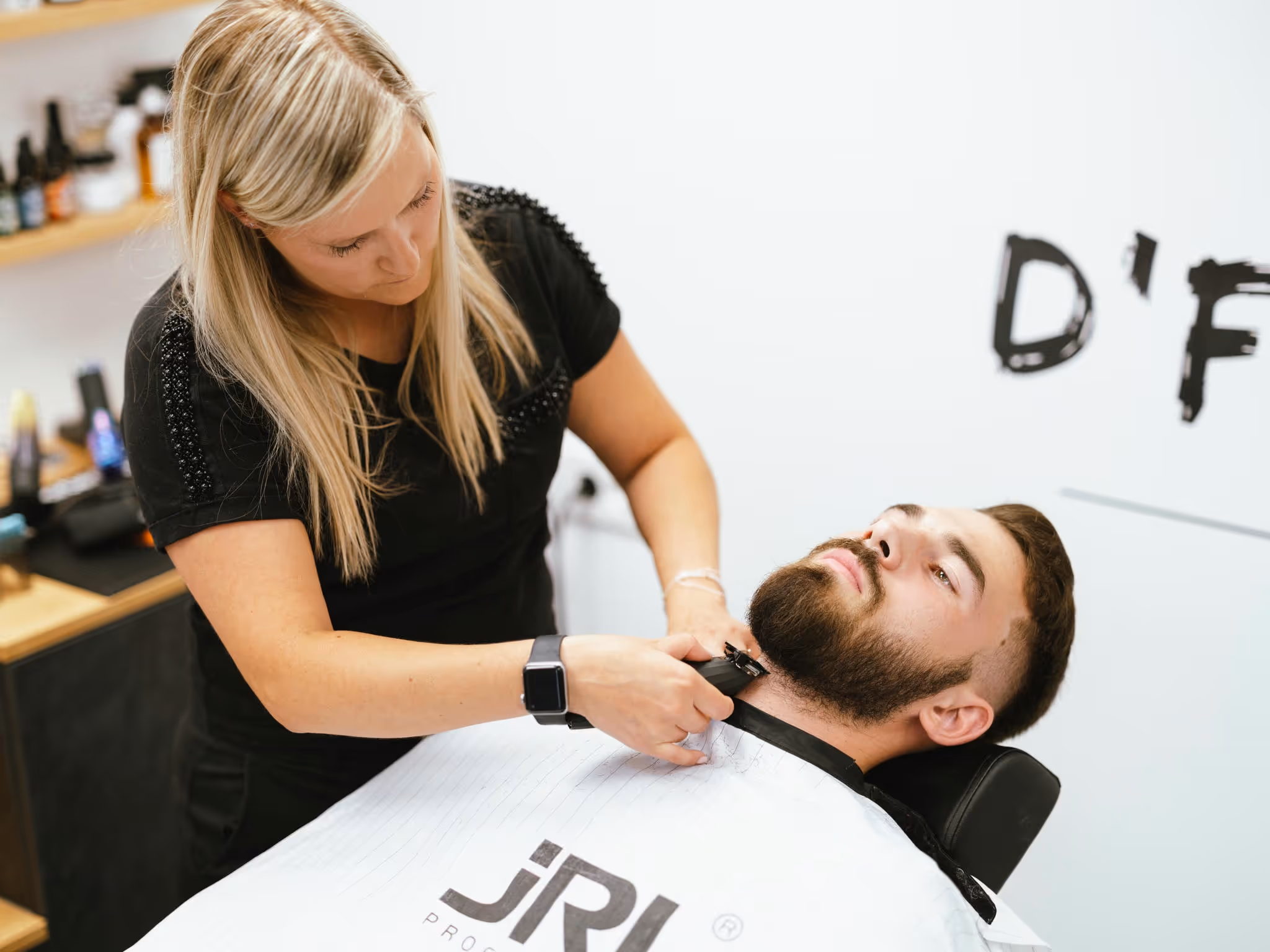 A man getting a shave from a woman with beard clippers